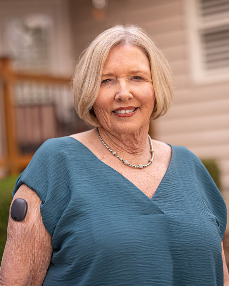 Eversense E3 user with CGM sensor and transmitter on her upper arm, outside house.
